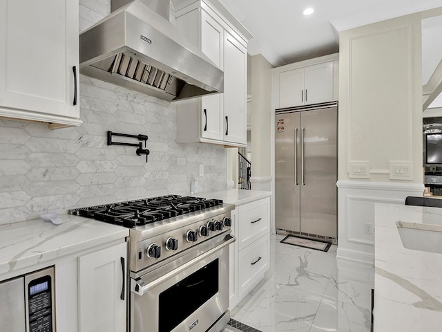 kitchen with light stone countertops, high quality appliances, wall chimney range hood, and white cabinets