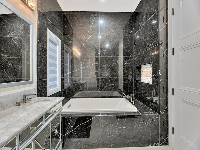 bathroom with vanity, a relaxing tiled tub, and tile walls