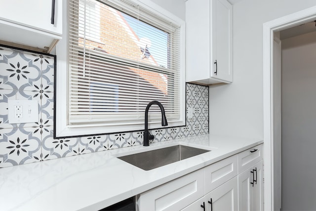 kitchen featuring tasteful backsplash, white cabinetry, sink, and light stone counters