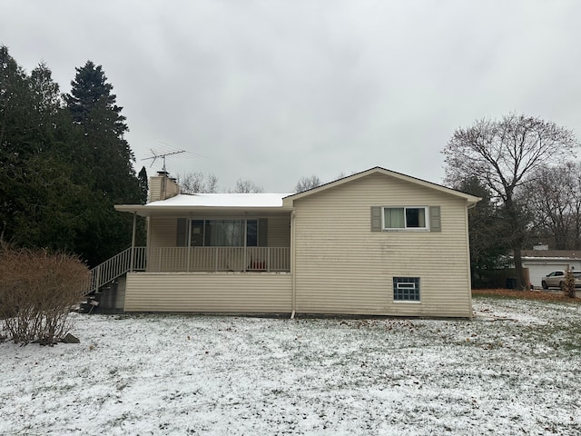 snow covered back of property with covered porch