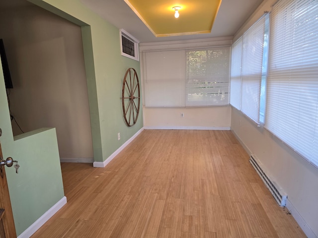 interior space featuring a tray ceiling, light hardwood / wood-style flooring, and baseboard heating