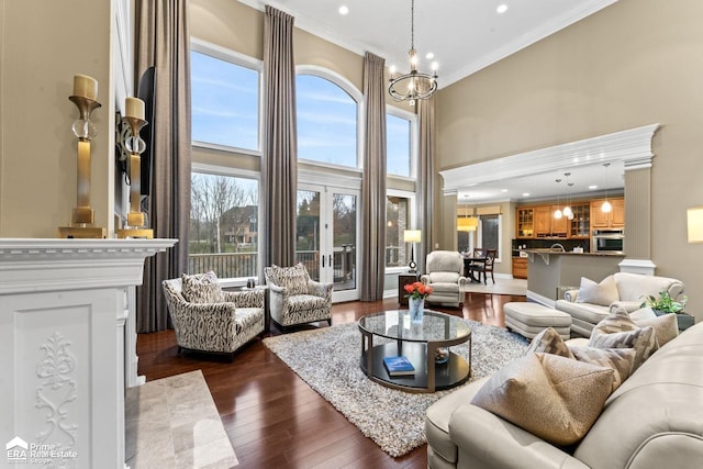 living room featuring french doors, a towering ceiling, ornamental molding, a chandelier, and dark hardwood / wood-style floors