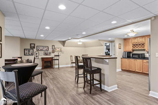 kitchen with light brown cabinetry, a paneled ceiling, light hardwood / wood-style floors, and a breakfast bar area