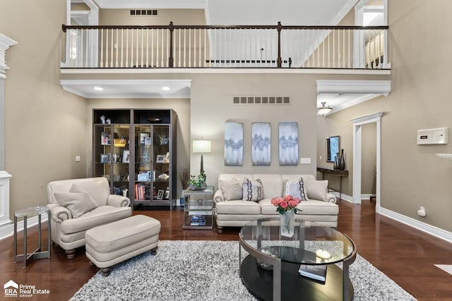 living room with dark hardwood / wood-style flooring, ornamental molding, and a towering ceiling