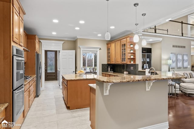 kitchen with light stone countertops, stainless steel appliances, kitchen peninsula, decorative light fixtures, and a kitchen bar