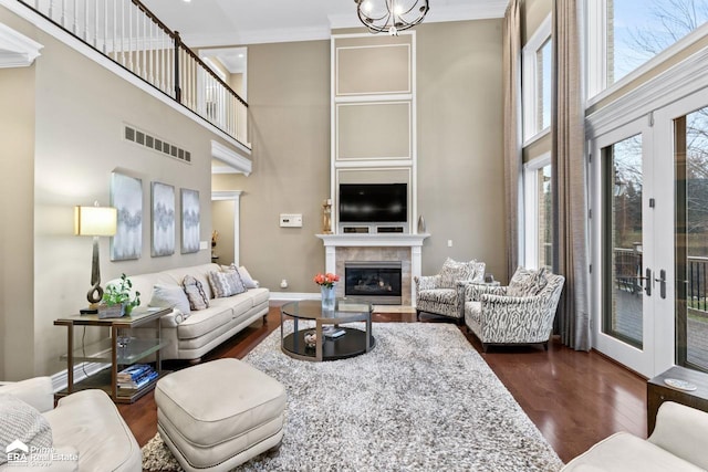 living room with french doors, a towering ceiling, dark hardwood / wood-style flooring, ornamental molding, and a tile fireplace