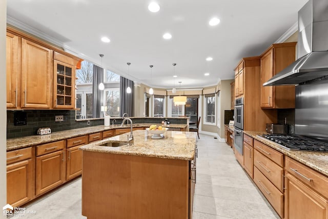 kitchen featuring appliances with stainless steel finishes, wall chimney range hood, sink, pendant lighting, and an island with sink