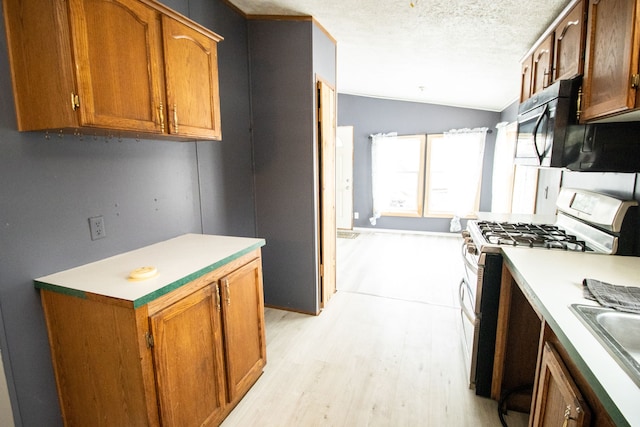 kitchen with vaulted ceiling, sink, white gas range oven, a textured ceiling, and light hardwood / wood-style flooring