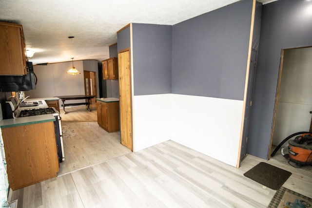 kitchen featuring gas range, light hardwood / wood-style floors, a textured ceiling, and pendant lighting