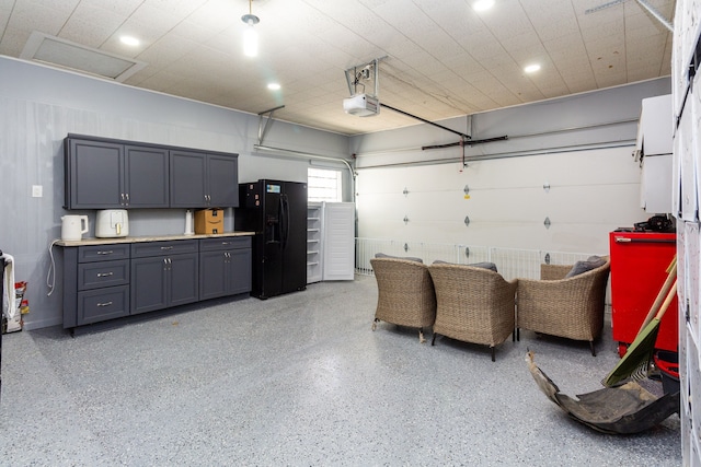 garage with black refrigerator with ice dispenser and a garage door opener