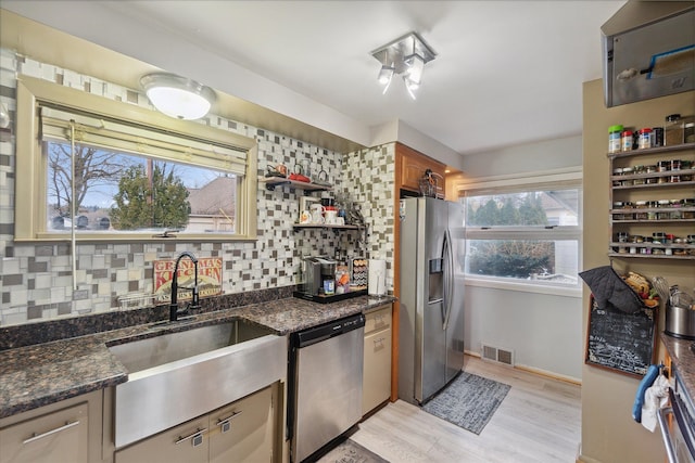 kitchen with sink, stainless steel appliances, dark stone counters, and light hardwood / wood-style flooring