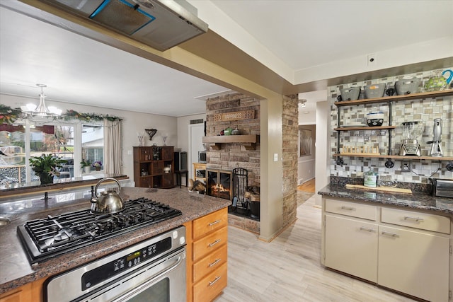 kitchen featuring an inviting chandelier, dark stone countertops, a fireplace, appliances with stainless steel finishes, and light hardwood / wood-style floors