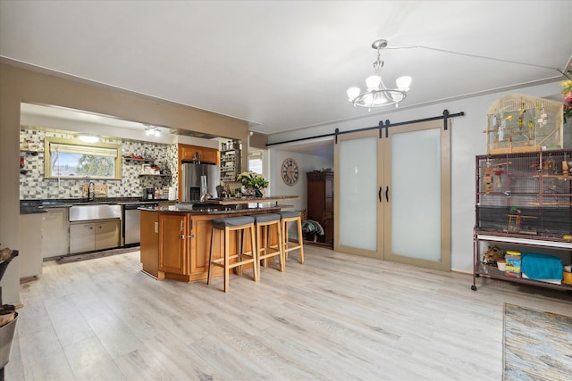 kitchen with a kitchen breakfast bar, hanging light fixtures, a barn door, appliances with stainless steel finishes, and tasteful backsplash