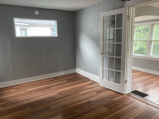 empty room featuring a textured ceiling, plenty of natural light, and dark wood-type flooring