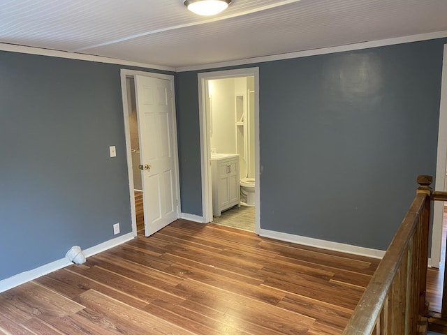 unfurnished bedroom featuring hardwood / wood-style floors, ensuite bathroom, a closet, and crown molding