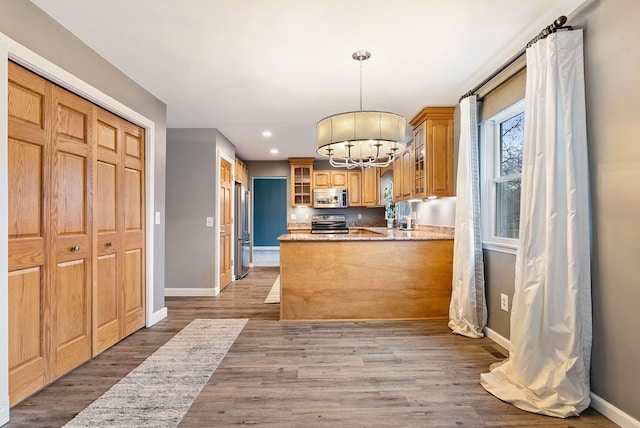 kitchen with a notable chandelier, kitchen peninsula, pendant lighting, appliances with stainless steel finishes, and light wood-type flooring