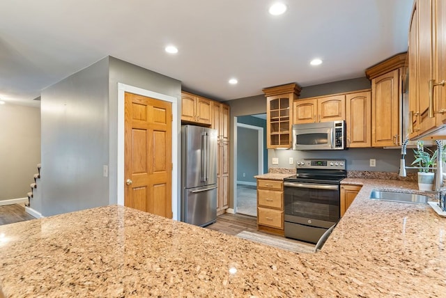 kitchen featuring light stone counters, sink, light hardwood / wood-style floors, and appliances with stainless steel finishes