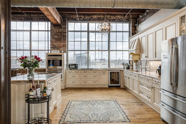 kitchen with beam ceiling, sink, beverage cooler, appliances with stainless steel finishes, and light wood-type flooring