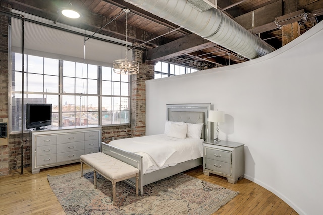 bedroom with light hardwood / wood-style floors, a towering ceiling, brick wall, and multiple windows