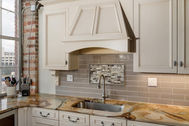 kitchen with decorative backsplash, white cabinetry, sink, and light stone countertops