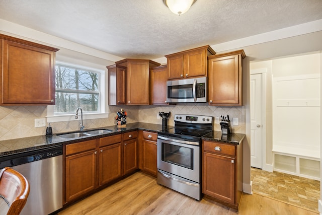 kitchen featuring decorative backsplash, appliances with stainless steel finishes, sink, dark stone countertops, and light hardwood / wood-style floors