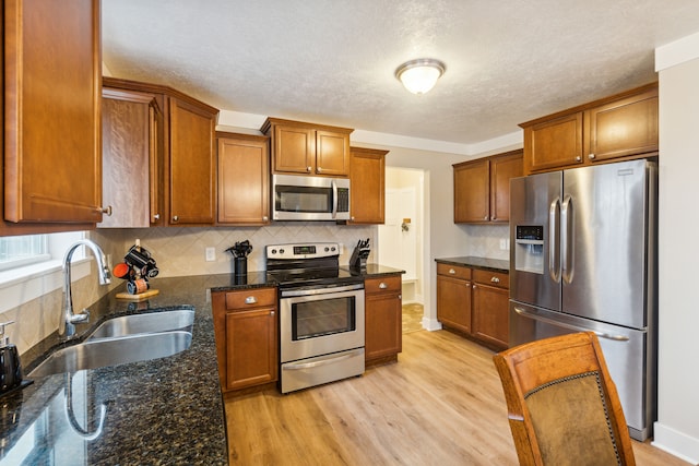 kitchen featuring light wood-type flooring, stainless steel appliances, dark stone countertops, and sink