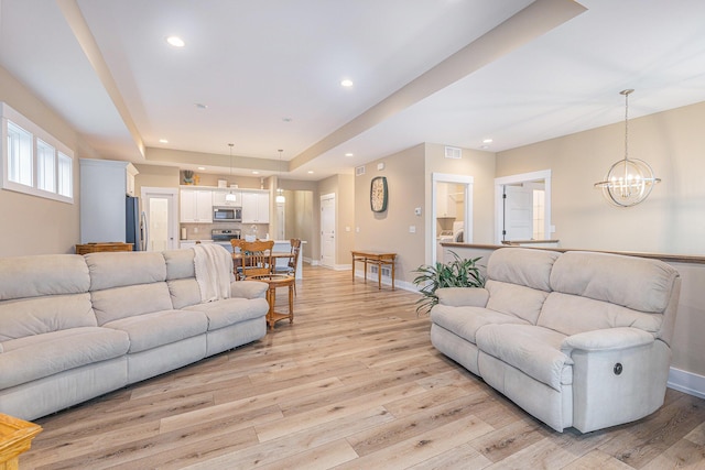 living room featuring a chandelier, light hardwood / wood-style flooring, and a raised ceiling