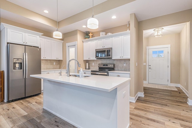 kitchen with a center island with sink, sink, white cabinetry, hanging light fixtures, and stainless steel appliances