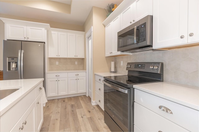 kitchen featuring white cabinets, decorative backsplash, appliances with stainless steel finishes, and light hardwood / wood-style floors