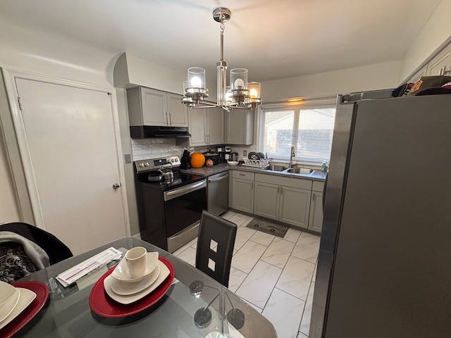 kitchen with appliances with stainless steel finishes, backsplash, sink, a chandelier, and gray cabinets