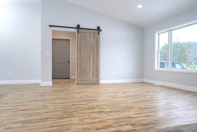 spare room featuring light wood-type flooring, a barn door, baseboards, and recessed lighting