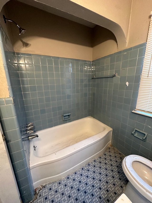 bathroom with tile patterned flooring, tiled shower / bath combo, tile walls, and toilet