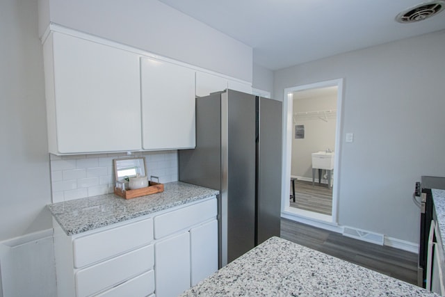 kitchen featuring light stone countertops, backsplash, dark wood-type flooring, white cabinets, and stainless steel refrigerator