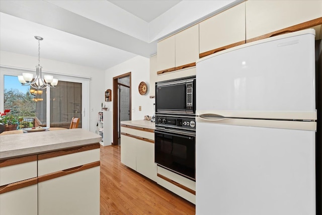 kitchen featuring black appliances, hanging light fixtures, light hardwood / wood-style flooring, a notable chandelier, and white cabinetry