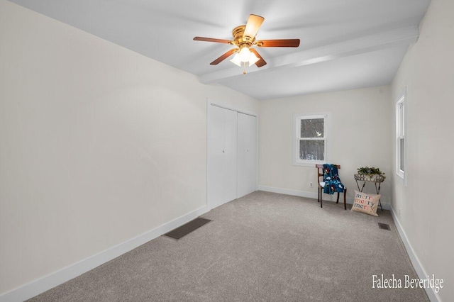 carpeted spare room featuring beamed ceiling and ceiling fan