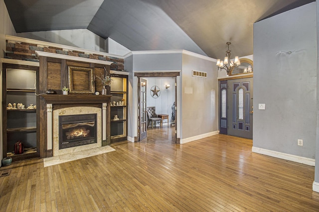 unfurnished living room featuring a notable chandelier, wood-type flooring, vaulted ceiling, a fireplace, and ornamental molding