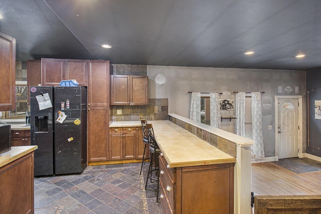 kitchen featuring kitchen peninsula, tasteful backsplash, black fridge, dark wood-type flooring, and a breakfast bar area