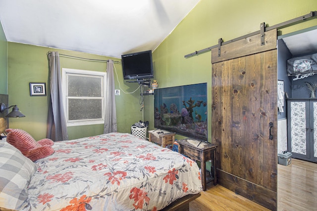 bedroom with lofted ceiling, a barn door, light hardwood / wood-style floors, and multiple windows