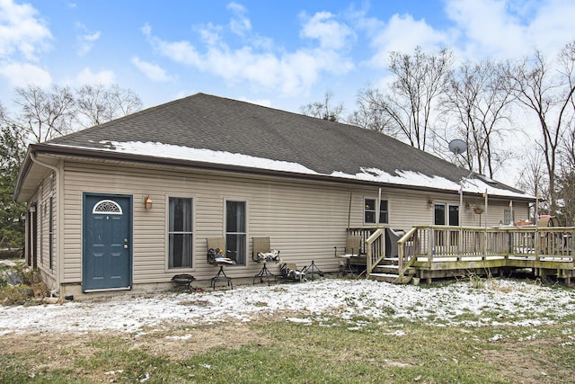 snow covered back of property with a wooden deck