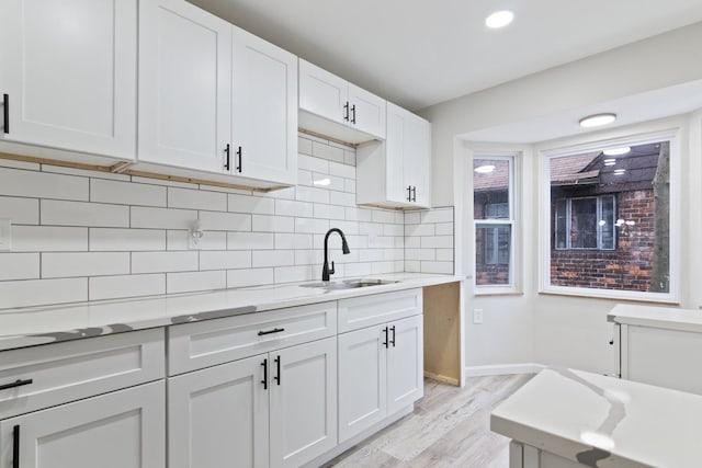 kitchen featuring decorative backsplash, light hardwood / wood-style floors, white cabinetry, and sink