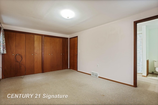 unfurnished bedroom featuring ensuite bathroom, light colored carpet, and a closet