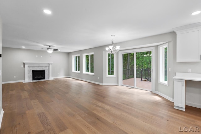 unfurnished living room with light wood-type flooring, a high end fireplace, a healthy amount of sunlight, and ceiling fan with notable chandelier