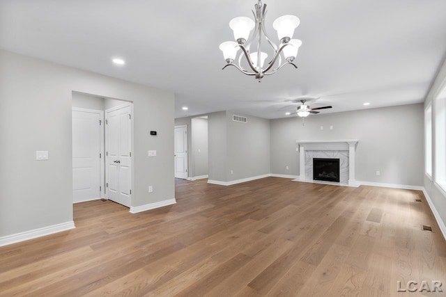 unfurnished living room with ceiling fan with notable chandelier, light hardwood / wood-style floors, and a fireplace