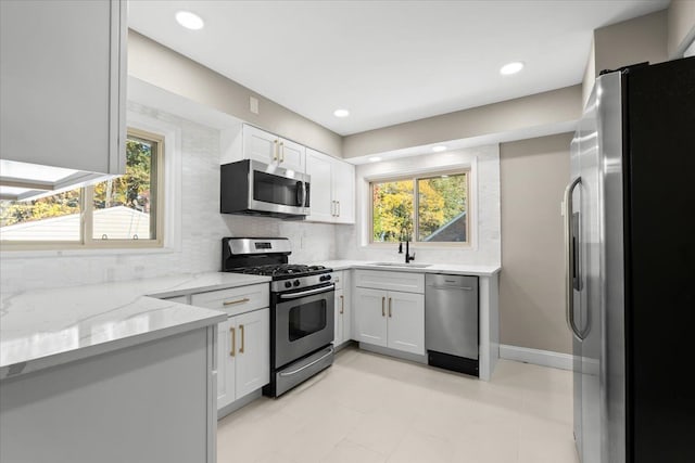 kitchen with a healthy amount of sunlight, light stone counters, white cabinetry, and appliances with stainless steel finishes