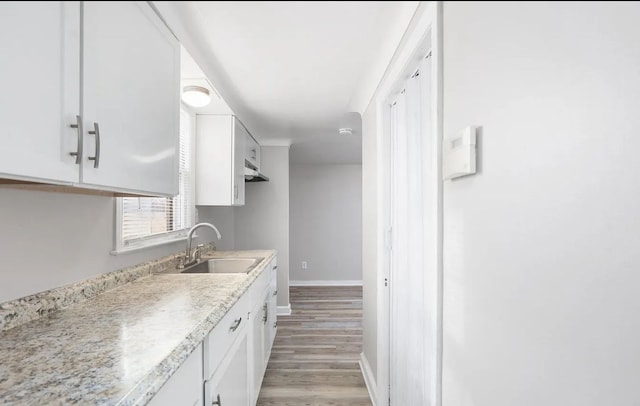 kitchen with light stone countertops, sink, white cabinets, and light wood-type flooring