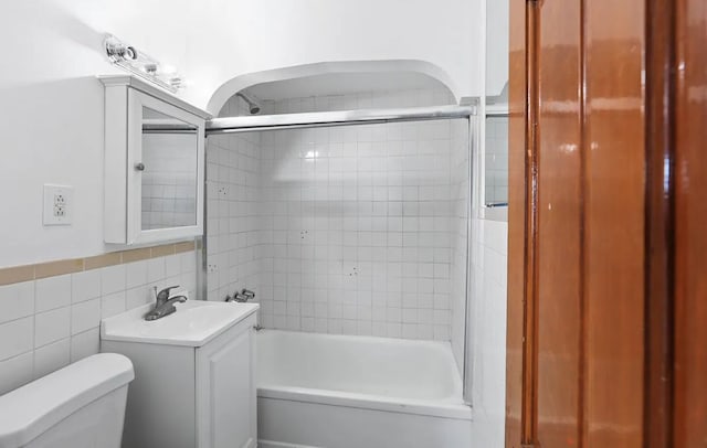 full bathroom featuring vanity, tiled shower / bath combo, tile walls, and toilet