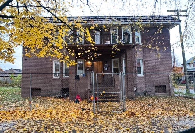 view of front of property featuring a balcony, a gate, fence, and brick siding