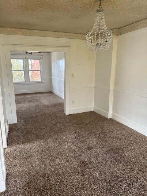 carpeted spare room with a chandelier and a textured ceiling