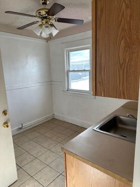 kitchen with light tile patterned floors, a textured ceiling, ceiling fan, and sink