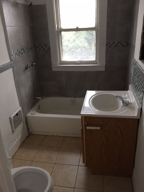 full bathroom featuring decorative backsplash, vanity, tiled shower / bath combo, tile patterned flooring, and toilet